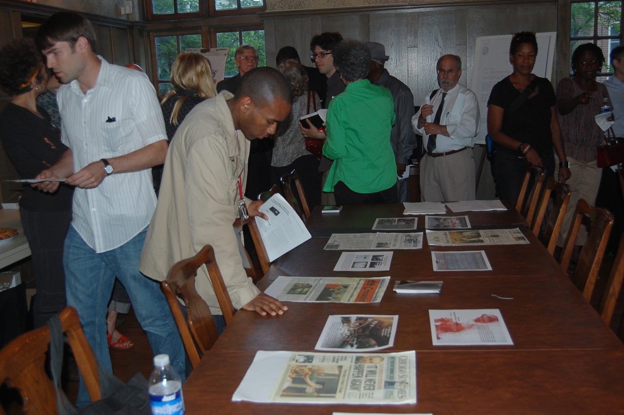 People buzz through a crowded room at the Jane Addams Hull House, gathering around a table covered in flyers and posters.