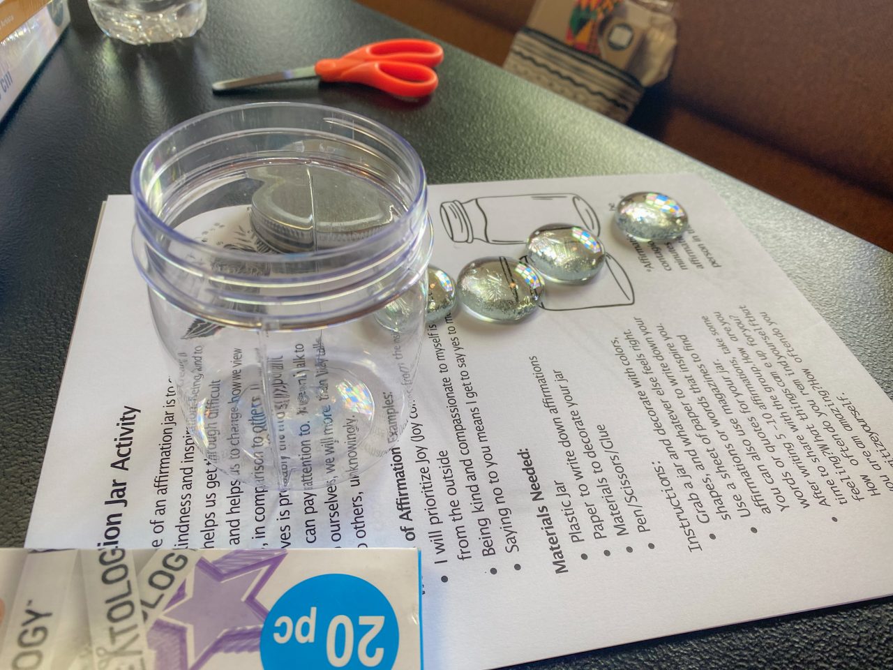 A glass jar, scissors, and glass beads on paper across a table